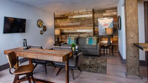 A dining area with a wooden table and chairs, a sofa, and a TV mounted on the wall.