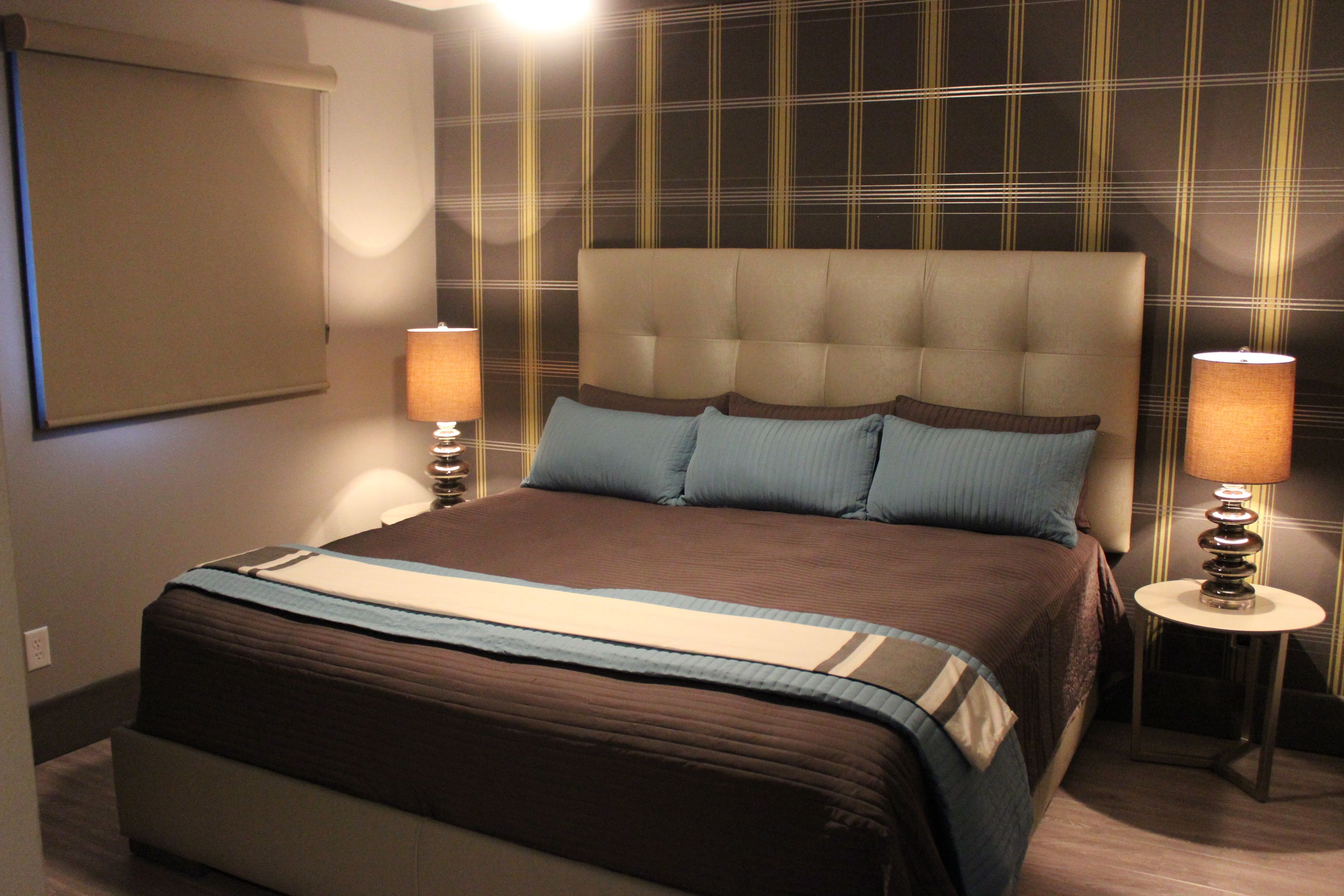A neatly made bed with a headboard, two bedside lamps, and a wall with a plaid pattern.