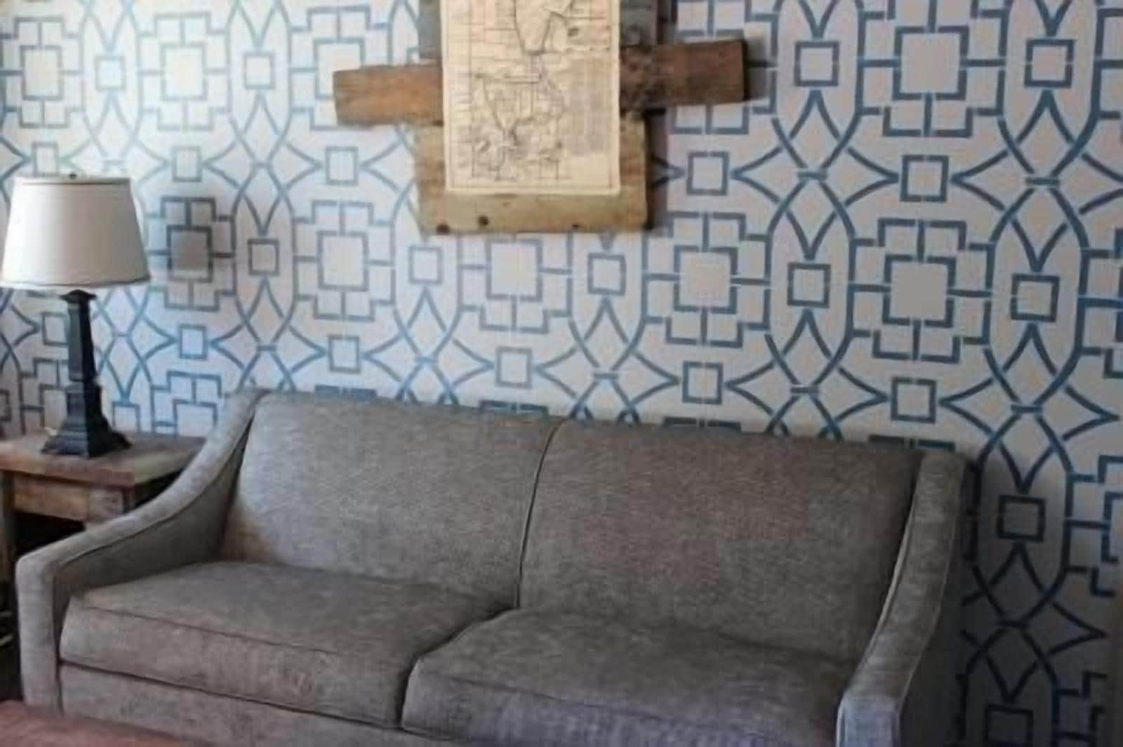 A gray sofa in a room with patterned wallpaper and a wooden cross.