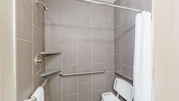 A shower area with a grab bar, a white chair, and a towel rack.