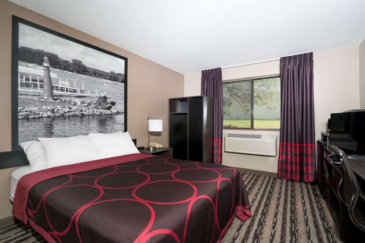 Une chambre d’hôtel avec un grand lit, une télévision, un bureau et une fenêtre avec des rideaux.