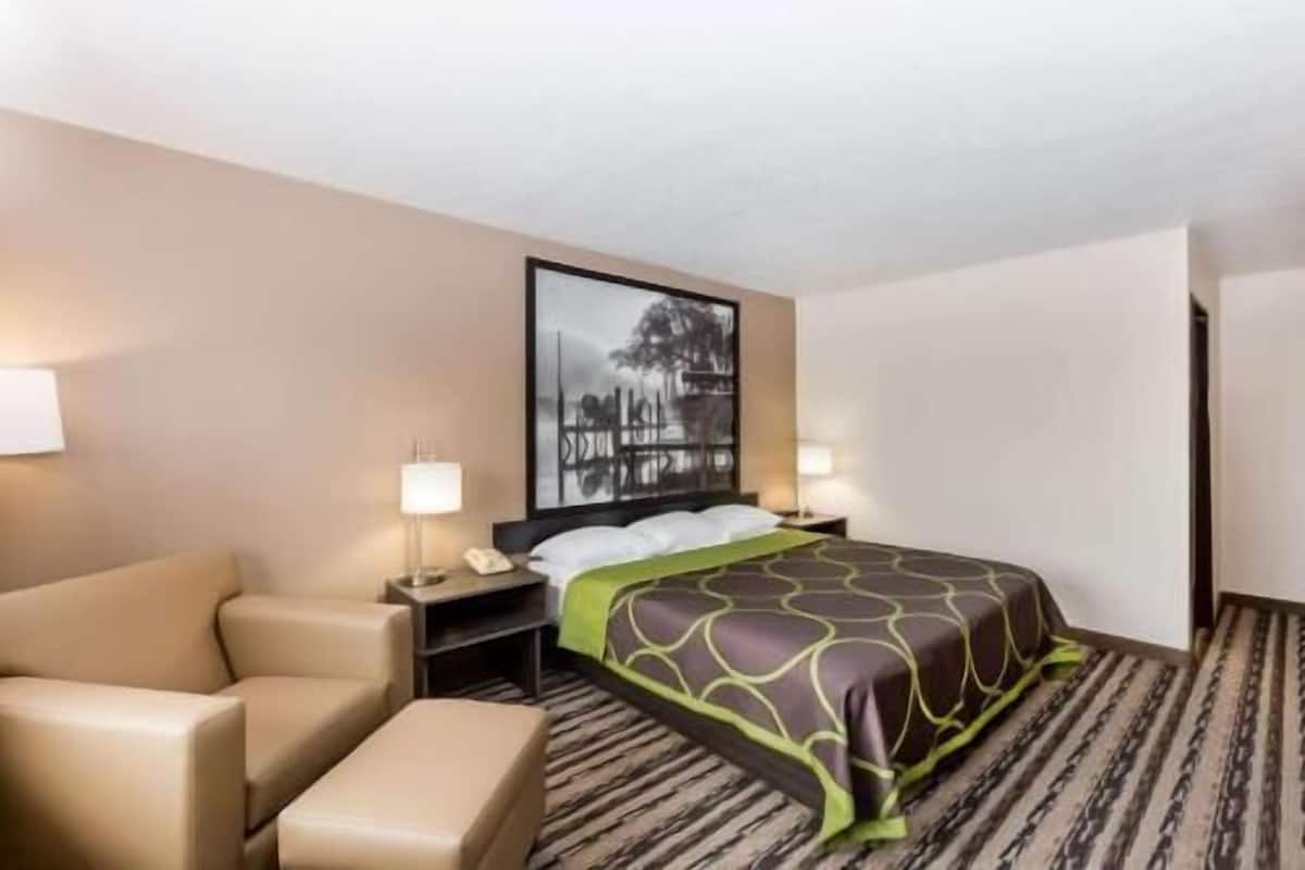 Une chambre d’hôtel comprenant un lit, une chaise, un bureau avec une lampe et une œuvre d’art accrochée au mur.