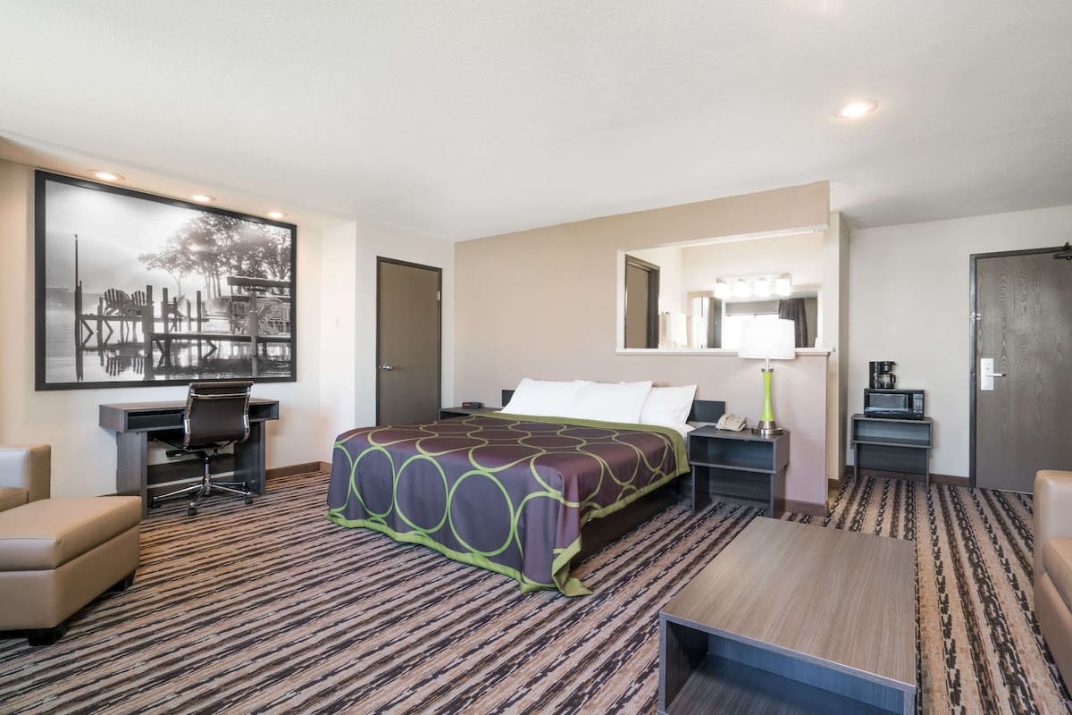 Une chambre d’hôtel avec un grand lit, un bureau avec une chaise, une petite table et un grand miroir.