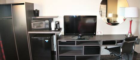 Una habitación de hotel compacta con kitchenette, un televisor de pantalla plana, un espejo y un escritorio con silla.