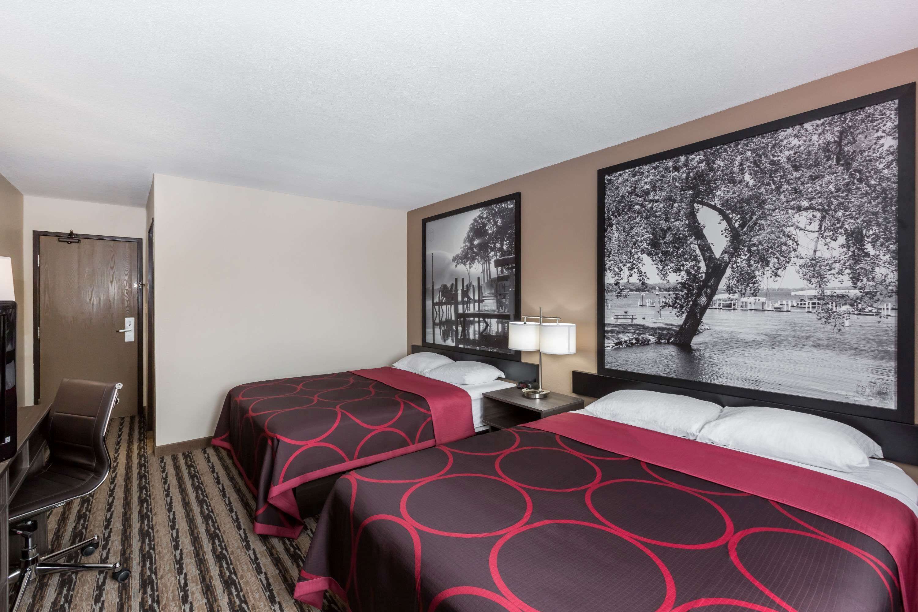 Habitación de hotel con dos camas, un escritorio y una silla. Hay dos cuadros grandes en la pared.