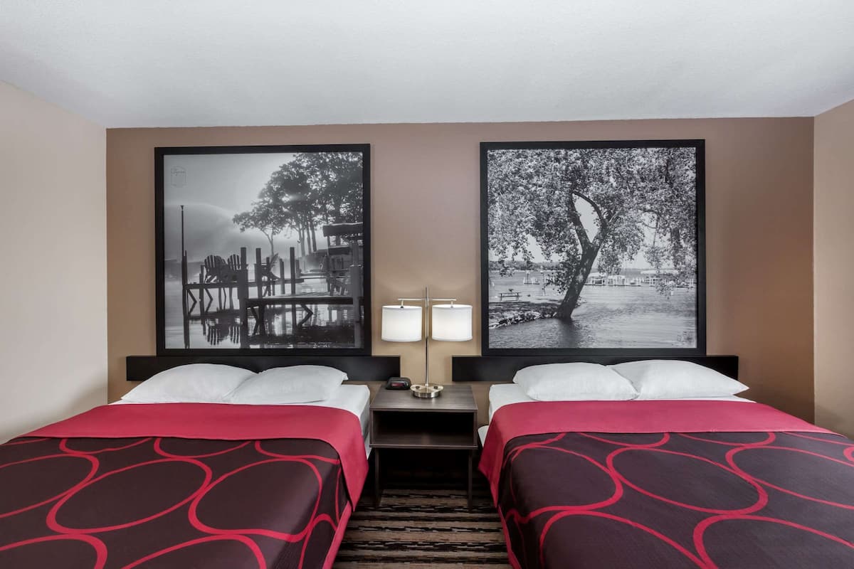 Une chambre d’hôtel avec deux lits, une table de chevet avec des lampes et deux photographies en noir et blanc encadrées accrochées au mur.