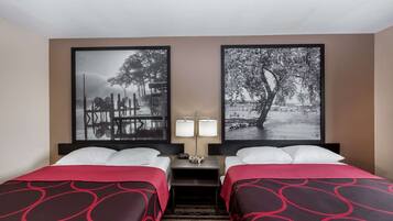 A hotel room with two beds, a nightstand with lamps, and two framed black-and-white photographs on the wall.