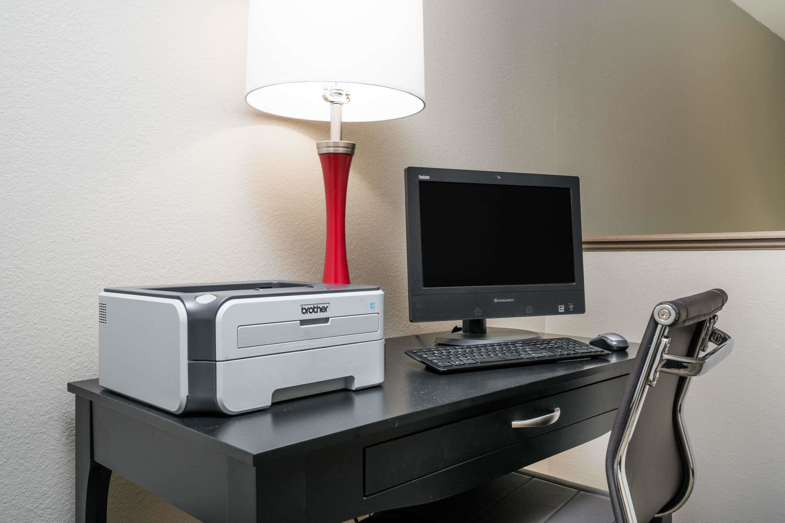 Ein Schreibtisch mit einem Brother-Drucker, einem Brother-Monitor, einer roten Lampe, einer Tastatur und einem schwarzen Stuhl.