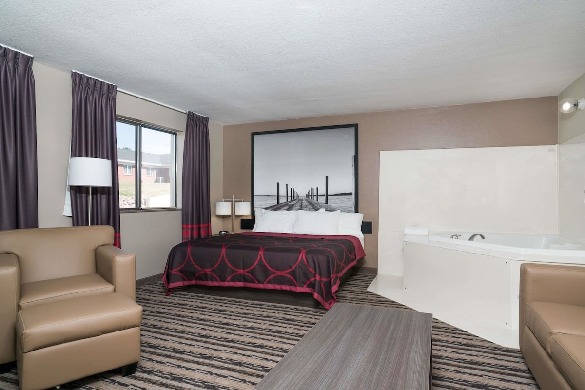Une chambre d’hôtel avec un lit, un canapé, un bureau, une baignoire et une grande fenêtre avec des rideaux.