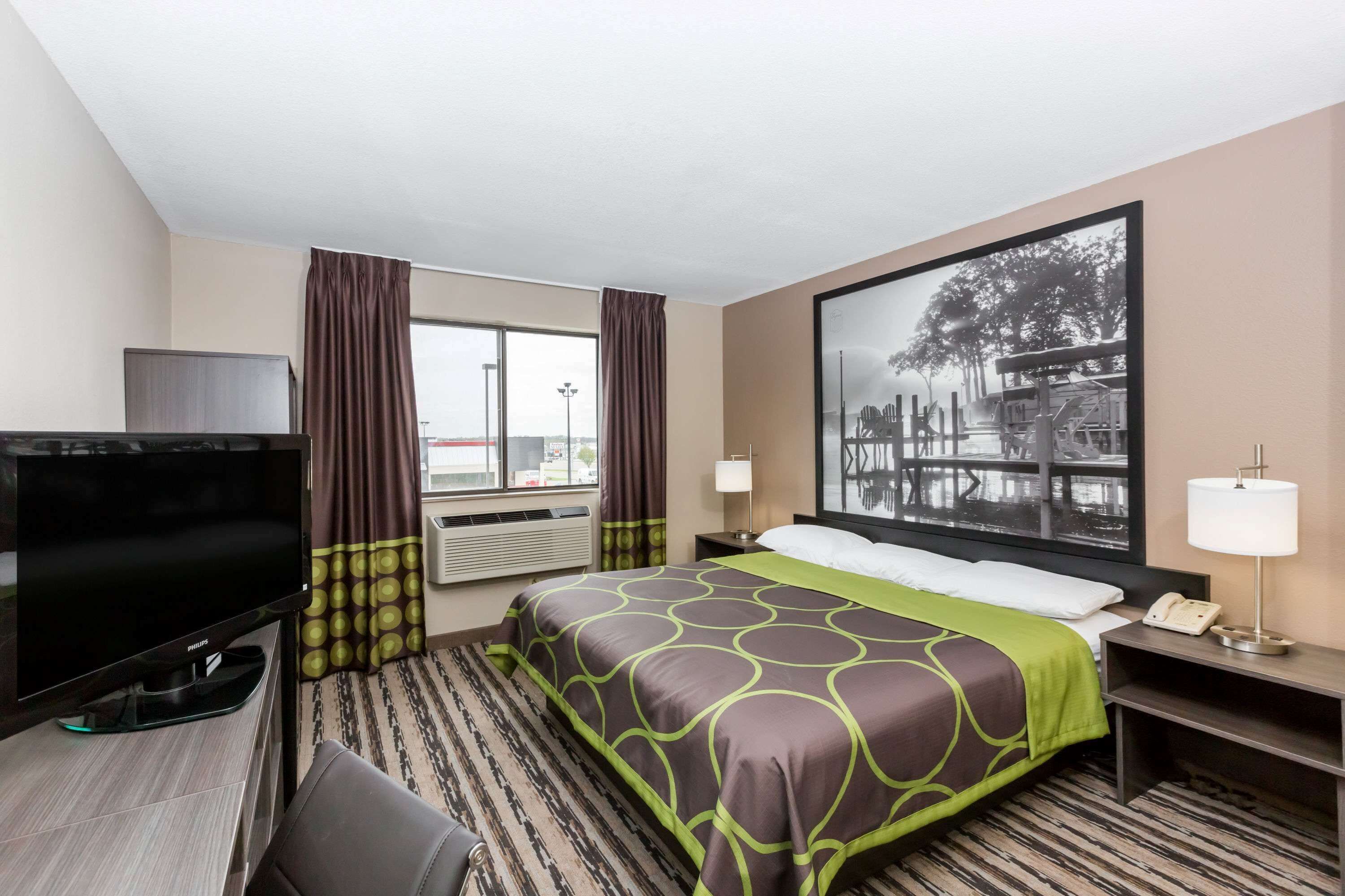 A hotel room with a bed, a flat-screen TV, a desk, and a large window.
