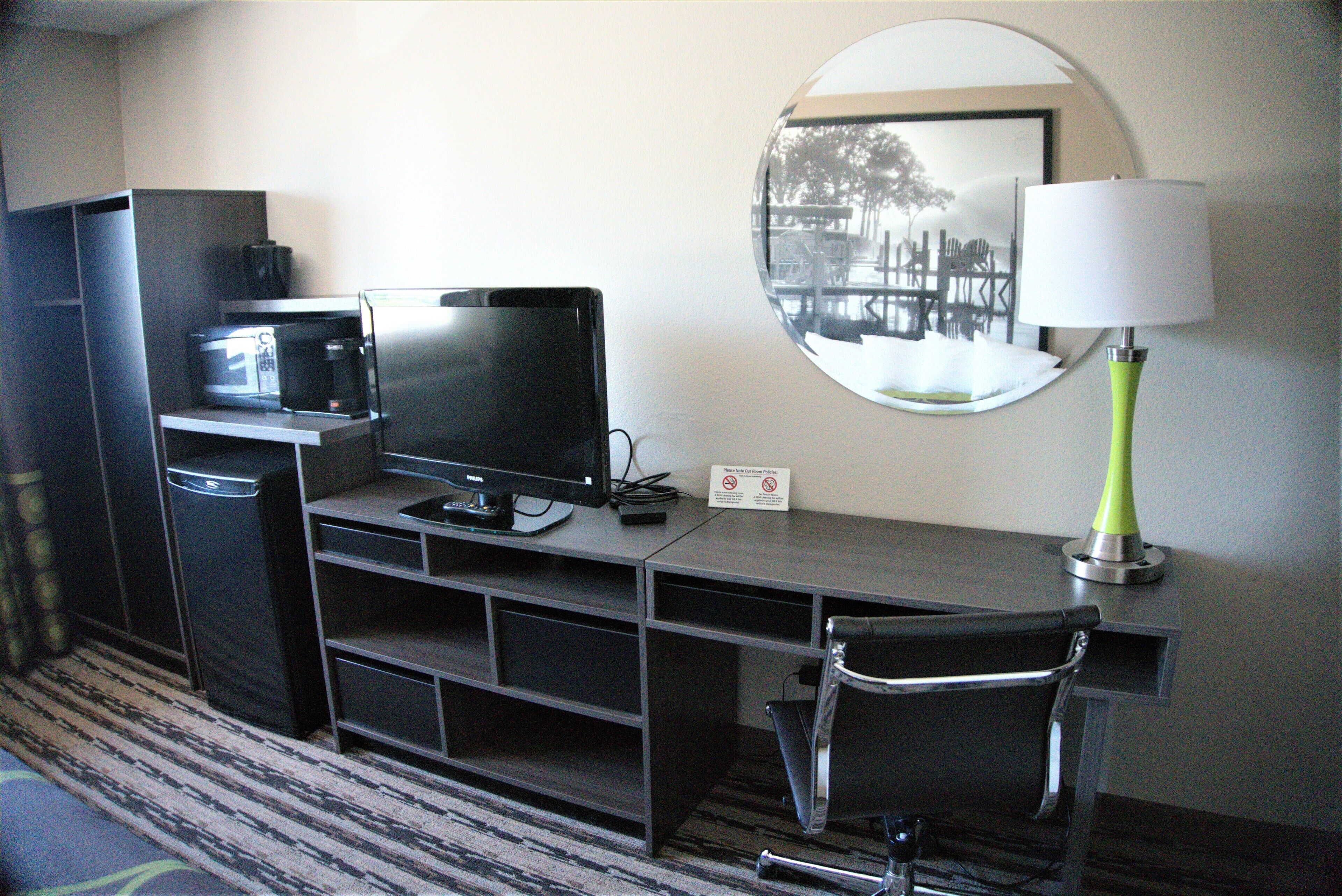 Habitación de hotel con escritorio, ordenador, silla, lámpara, microondas y espejo.