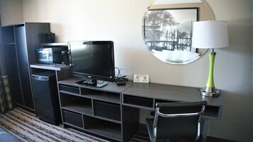 Habitación de hotel con escritorio, ordenador, silla, lámpara, microondas y espejo.