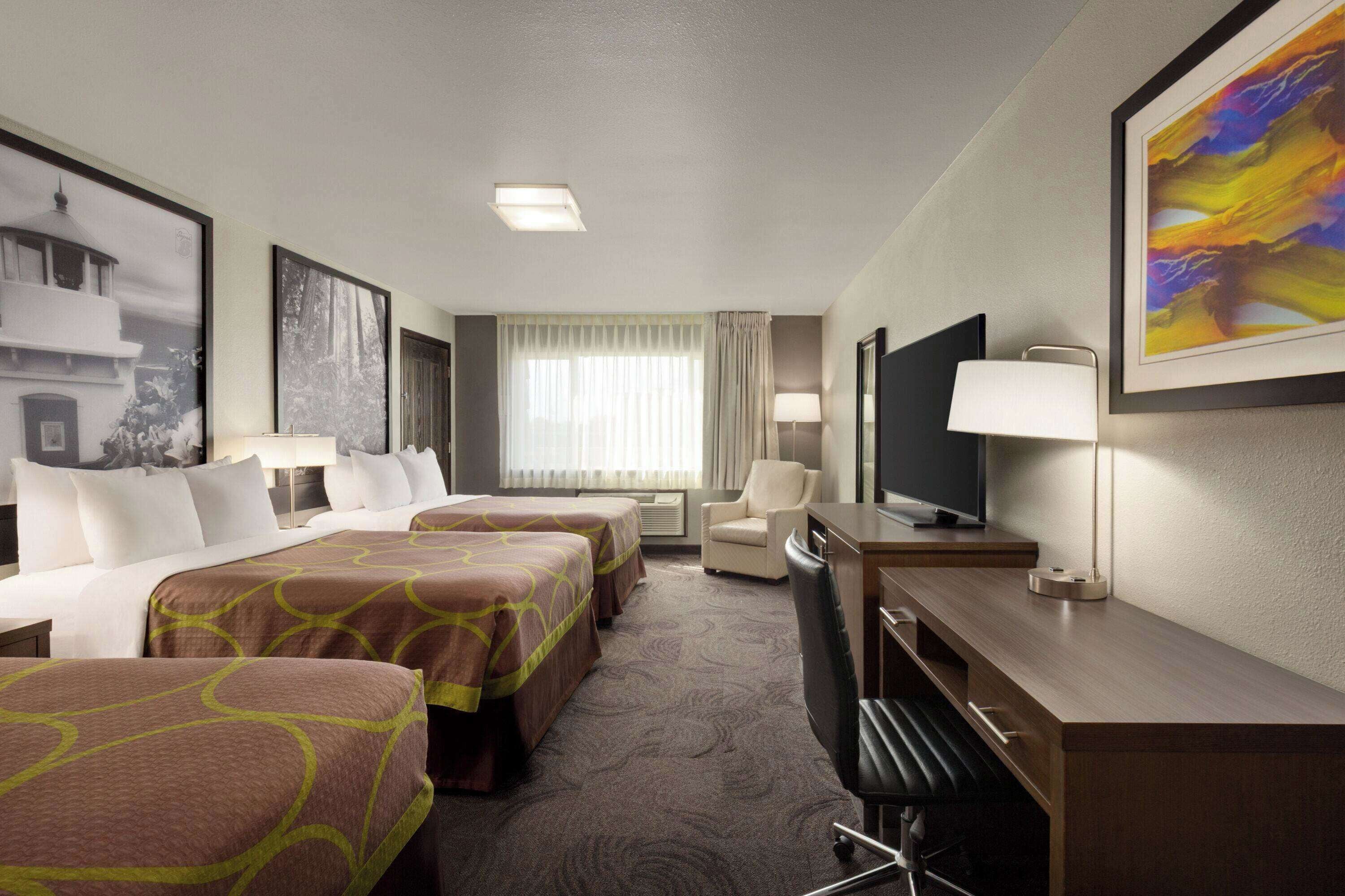 A hotel room with two beds, a desk, a chair, a TV, and a window with curtains.