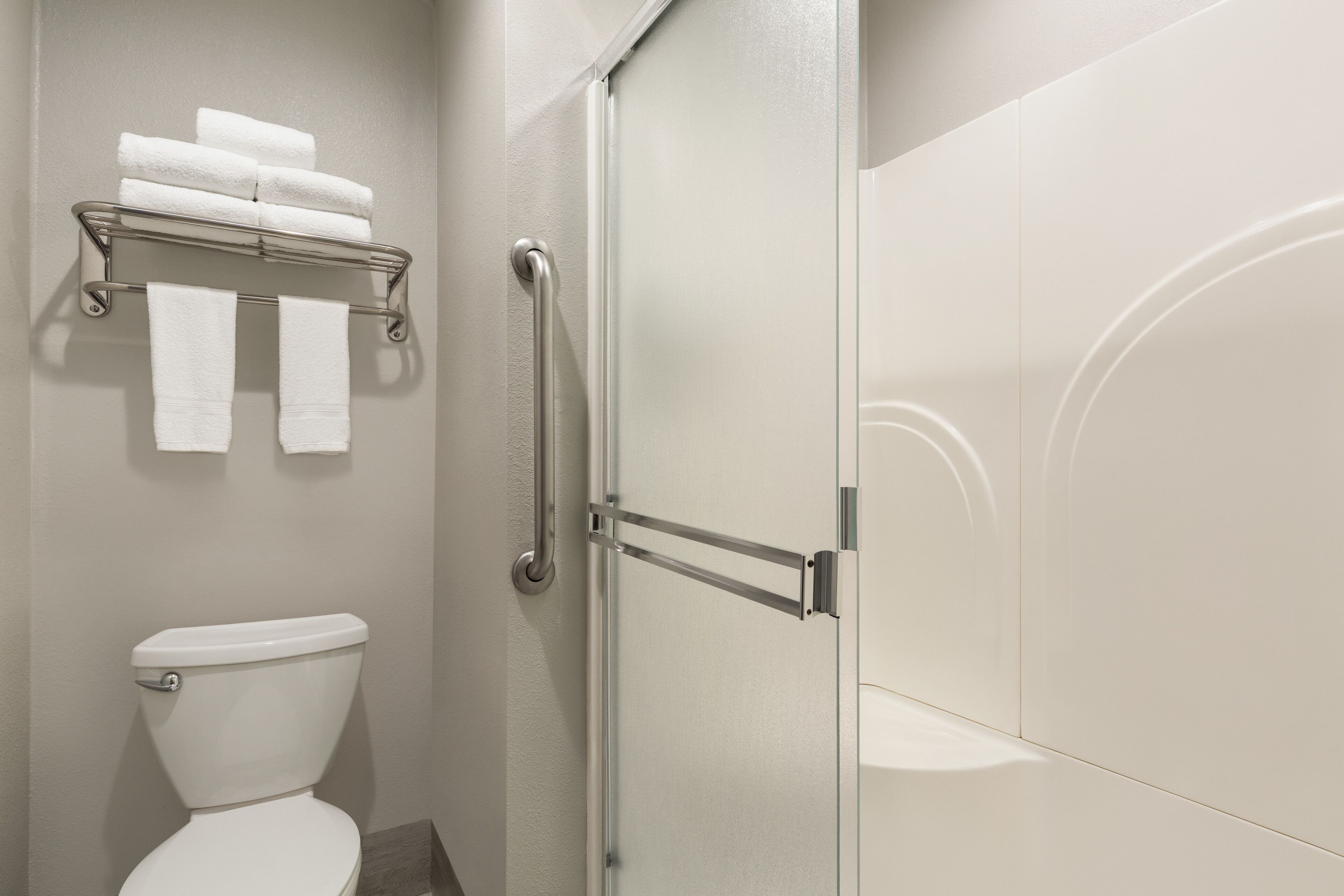 A bathroom with a toilet, a towel rack with folded towels, and a glass shower door.