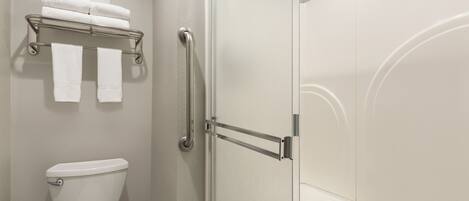 A bathroom with a toilet, a towel rack with folded towels, and a glass shower door.