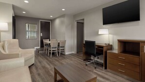Una sala de estar moderna con un sofá, una mesa de comedor con sillas, un escritorio con una computadora y un televisor montado en la pared.