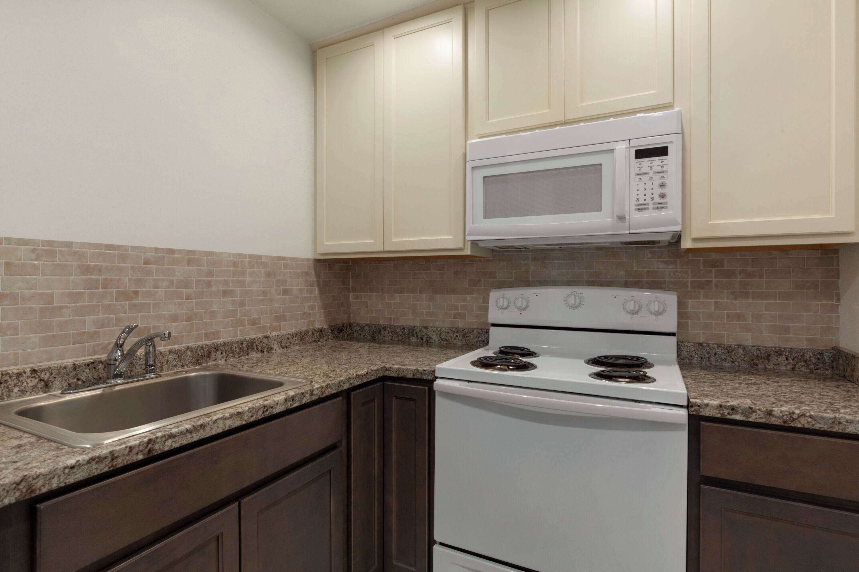 A kitchen with a white stove, a microwave, a sink, and dark brown cabinets.