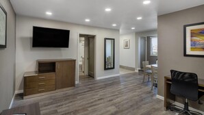 Una habitación amplia con televisión de pantalla plana, muebles de madera, zona de comedor y un espejo grande.