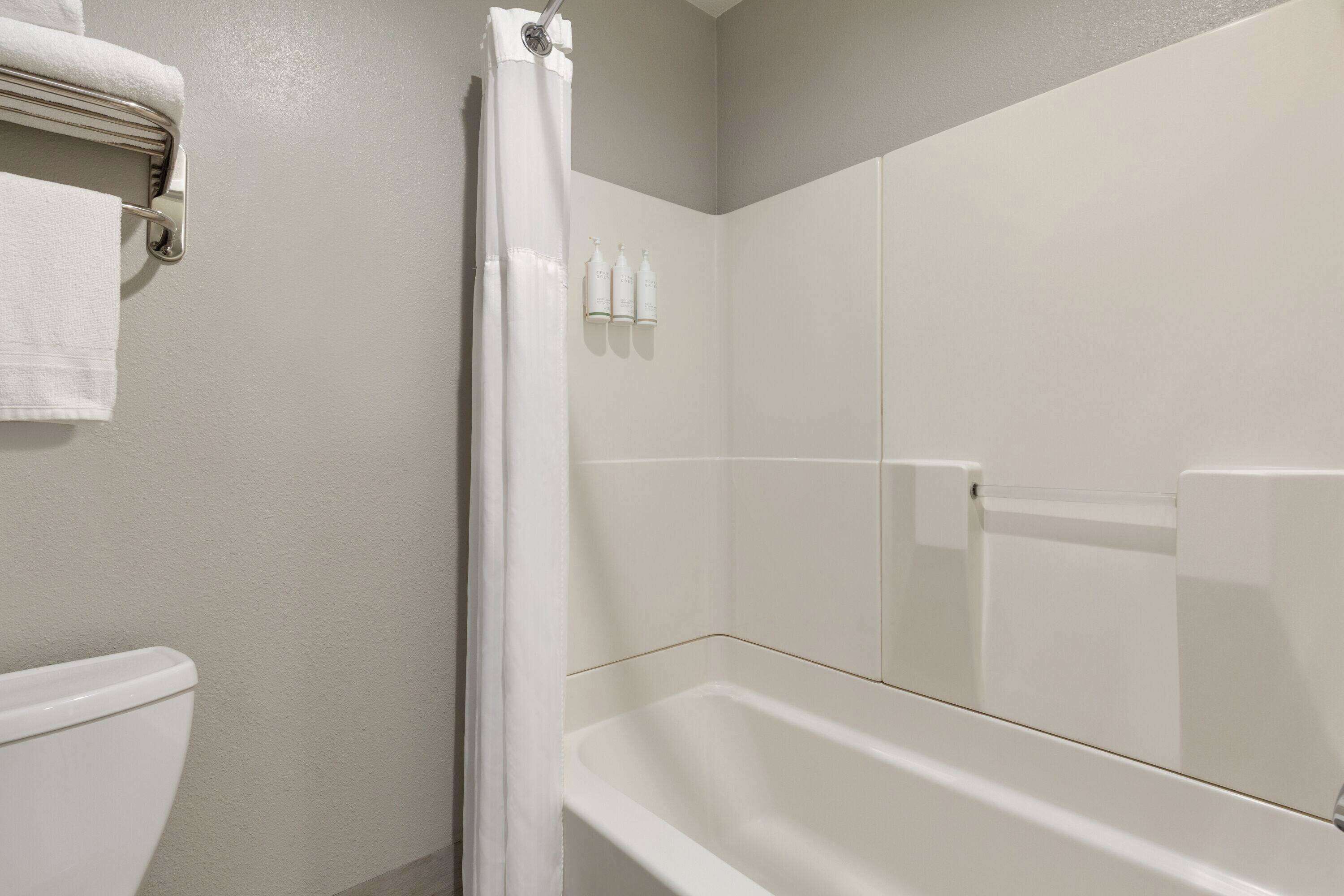 Een badkamer met een witte badkuip, een douchegordijn en een toilet. Drie flessen toiletartikelen staan op de muur.