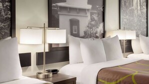 Habitación de hotel con dos camas, cada una con ropa blanca y una colcha marrón estampada. Hay dos mesitas de noche con lámparas, y las paredes están decoradas con fotografías blanco y negro enmarcadas.