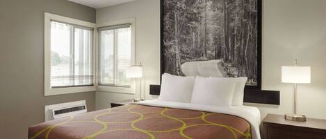A hotel room with a large bed, two bedside tables, a nightstand, a large framed picture on the wall, and a window with blinds.