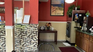 Ein Restaurantinnenraum mit einer gefliesten Spritzschutzwand, einem Holztisch und Stühlen. Es gibt eine Theke mit einer Speisekarte und einem Schild, einen Kühlschrank und eine Pflanze auf der Theke.