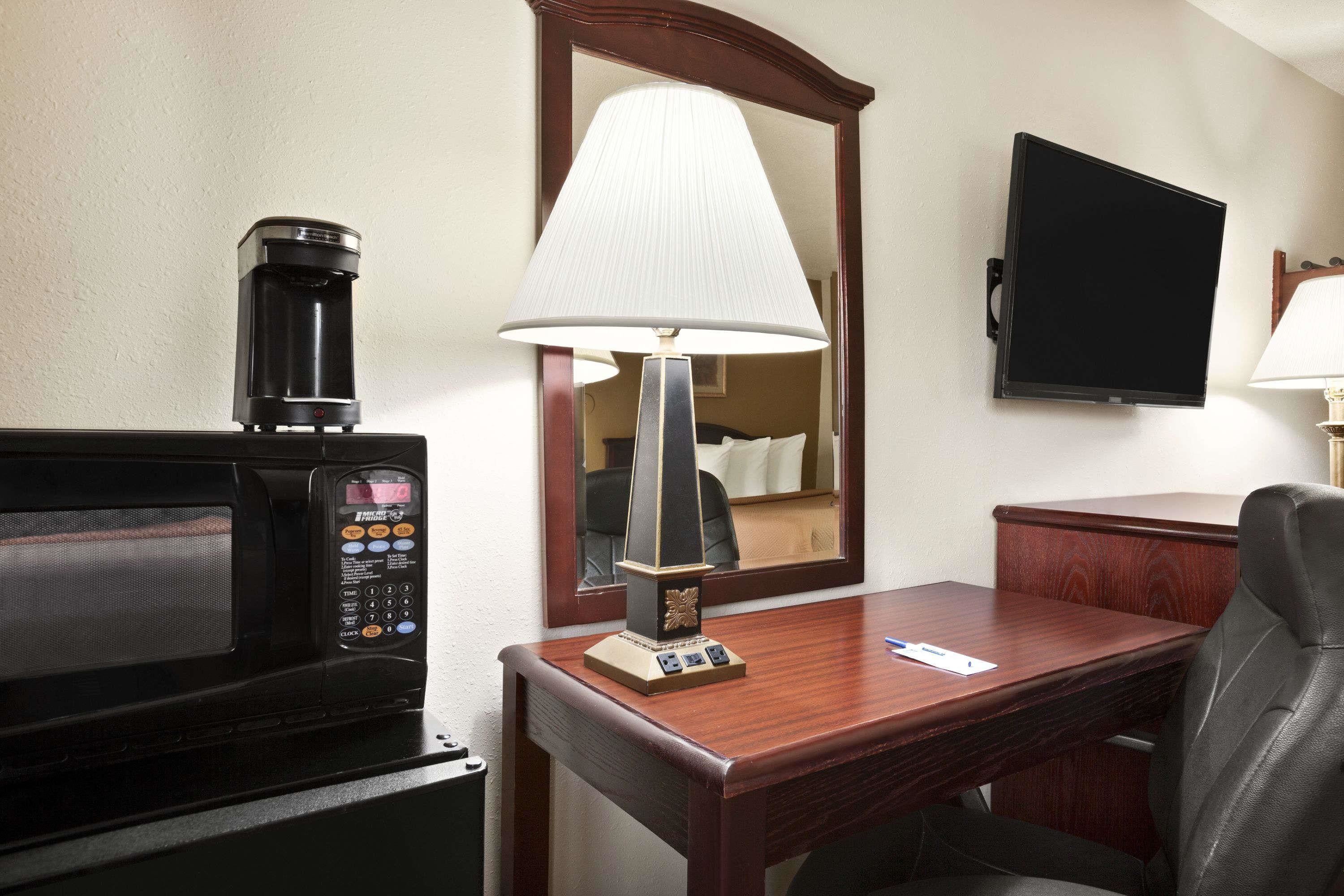 Habitación de hotel con microondas, lámpara, escritorio, silla y televisión.