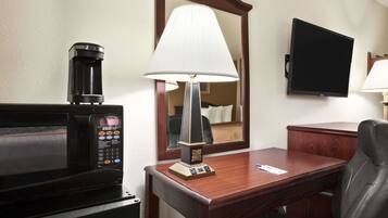 Habitación de hotel con microondas, lámpara, escritorio, silla y televisión.