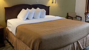 Ein Hotelzimmer mit einem großen Bett, zwei Nachttischlampen, einem gerahmten Bild an der Wand und einem Sessel am Fenster.