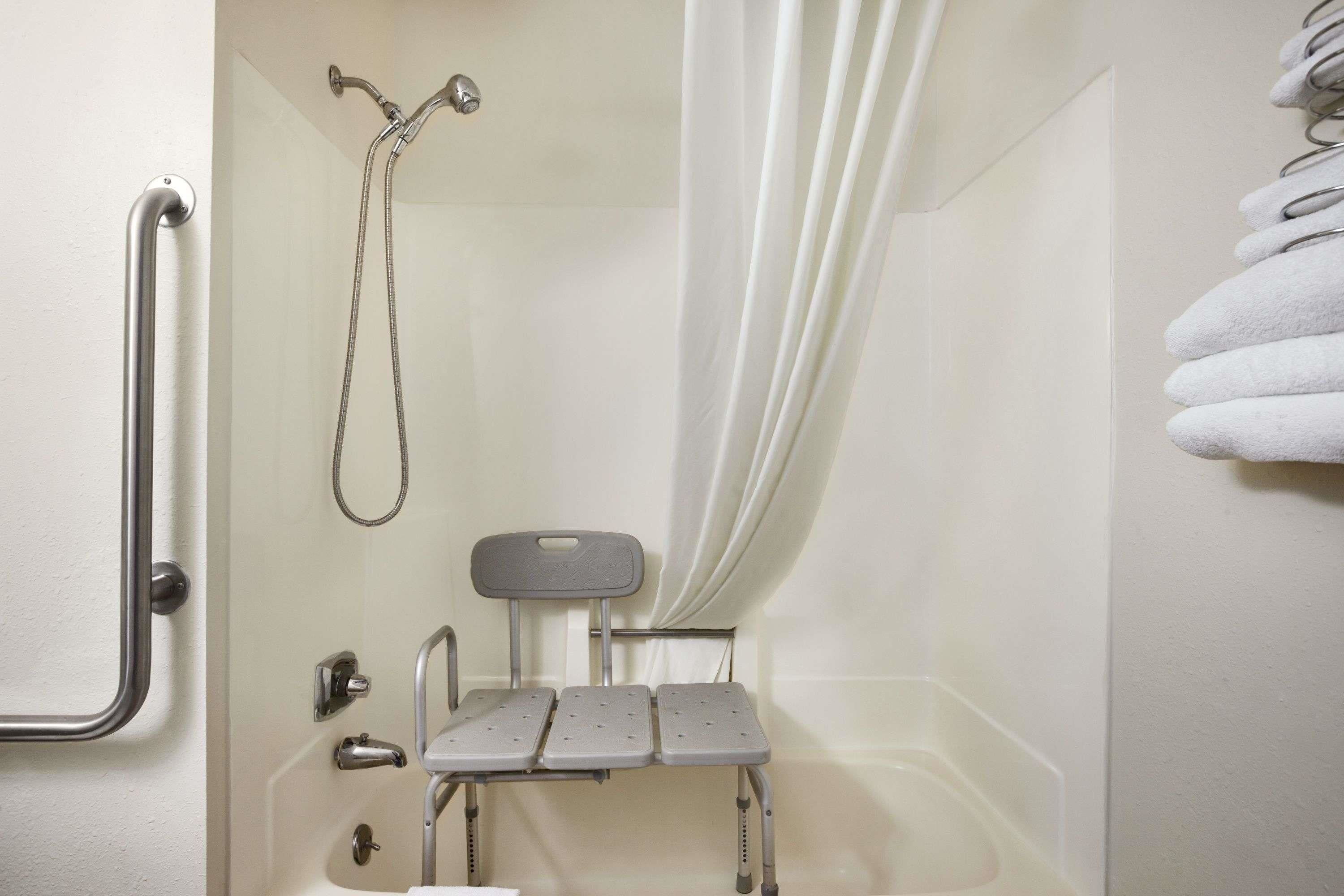 A bathroom with a shower, grab bars, a seat, and a towel rack.