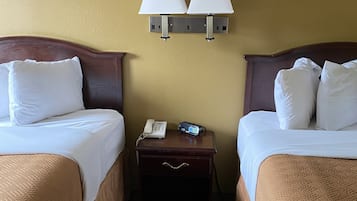 A hotel room with two beds, a nightstand with a phone and a remote, and two wall-mounted lamps.