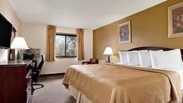 A hotel room with a large bed, two bedside tables, a desk, and a chair. There are two windows with curtains, and the walls are painted in a warm tone.