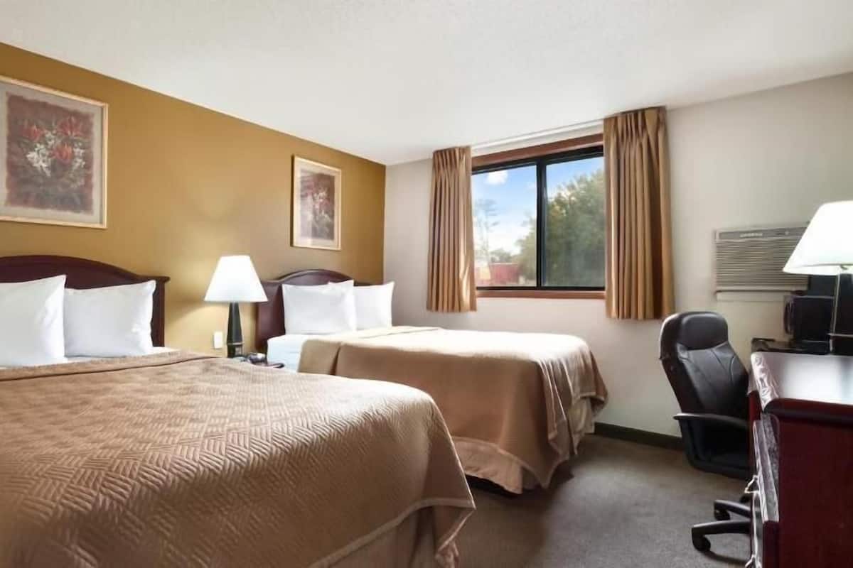 Une chambre d’hôtel avec deux lits, un bureau, une chaise et une fenêtre avec des rideaux.
