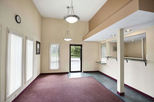 A hotel hallway with a red carpet, large windows, a clock, and a door leading outside.