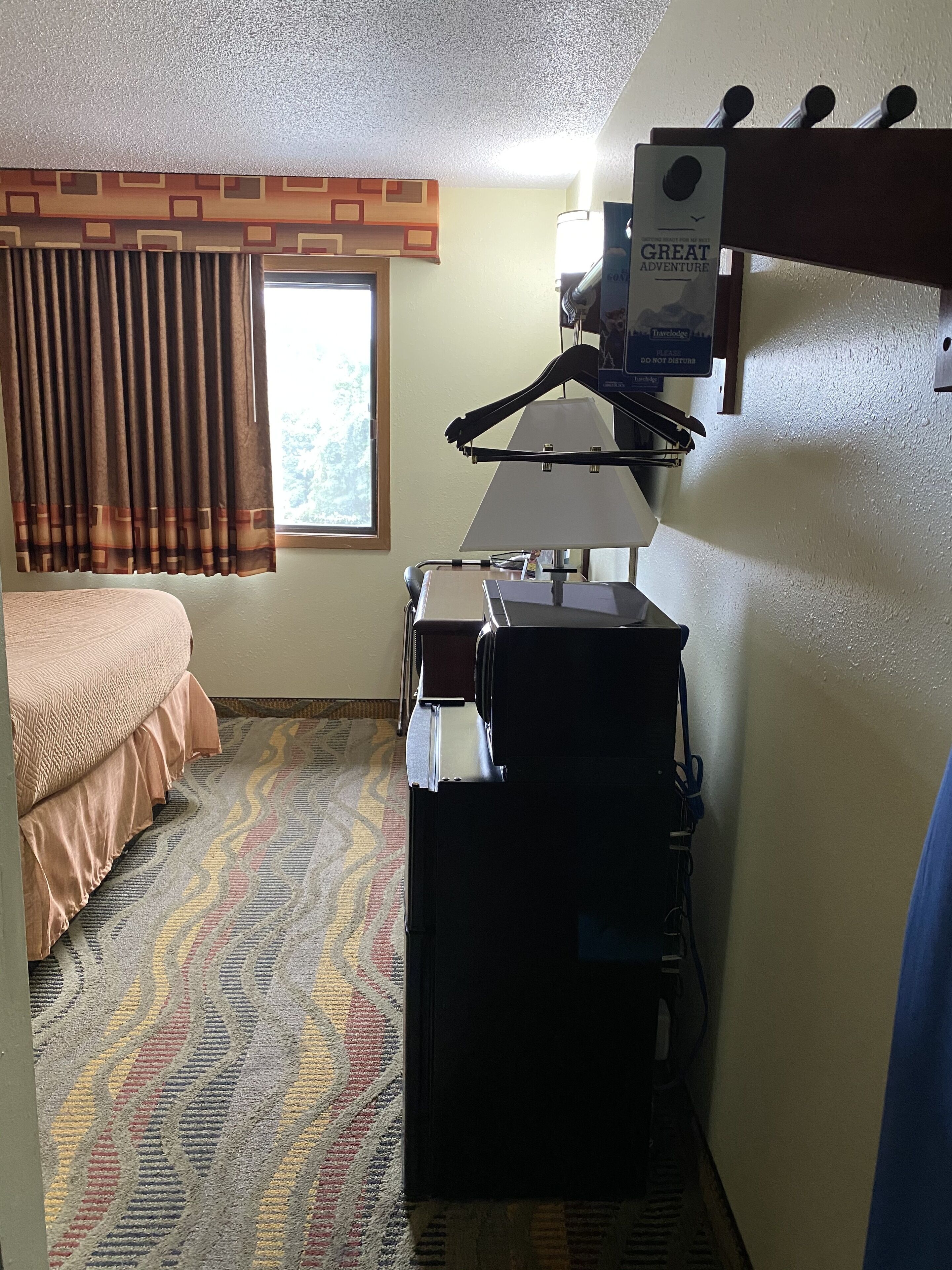 Une chambre d’hôtel équipée d’un lit, d’un bureau, d’une chaise, d’une lampe et d’un porte-manteau.