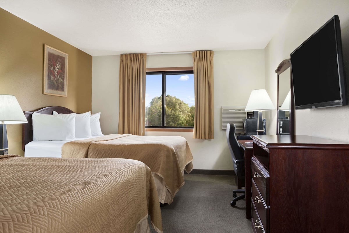 Une chambre d’hôtel avec deux lits, un bureau, une chaise, une télévision et une fenêtre avec des rideaux.