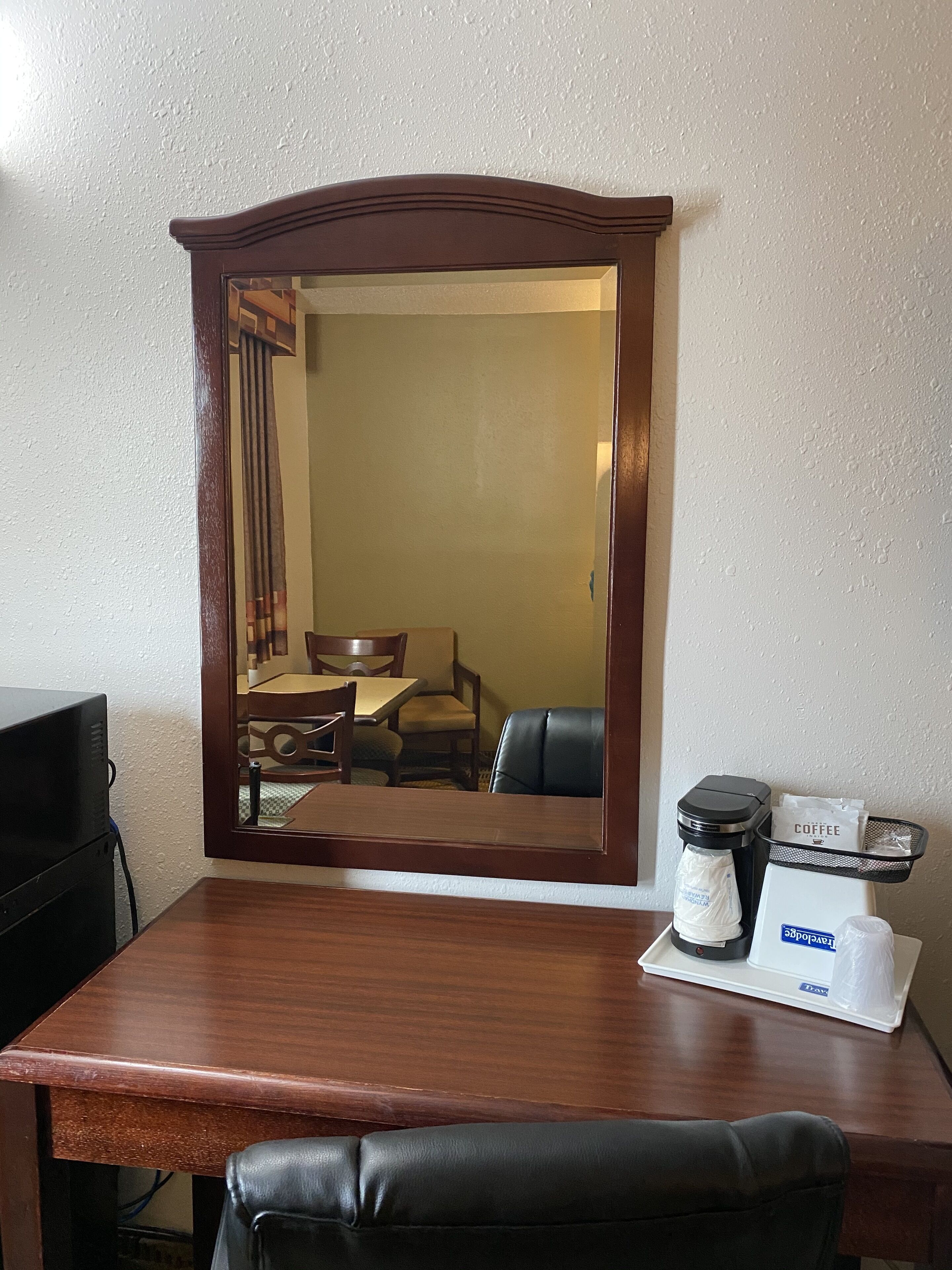A hotel room with a wooden desk, a coffee machine, and a tray with a coffee bag and a tray.
