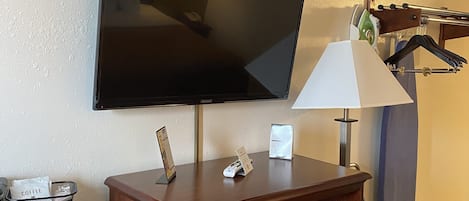 Une chambre d’hôtel équipée d’un téléviseur à écran plat fixé au mur, d’un bureau en bois avec un téléphone, une lampe et un petit coffre-fort.