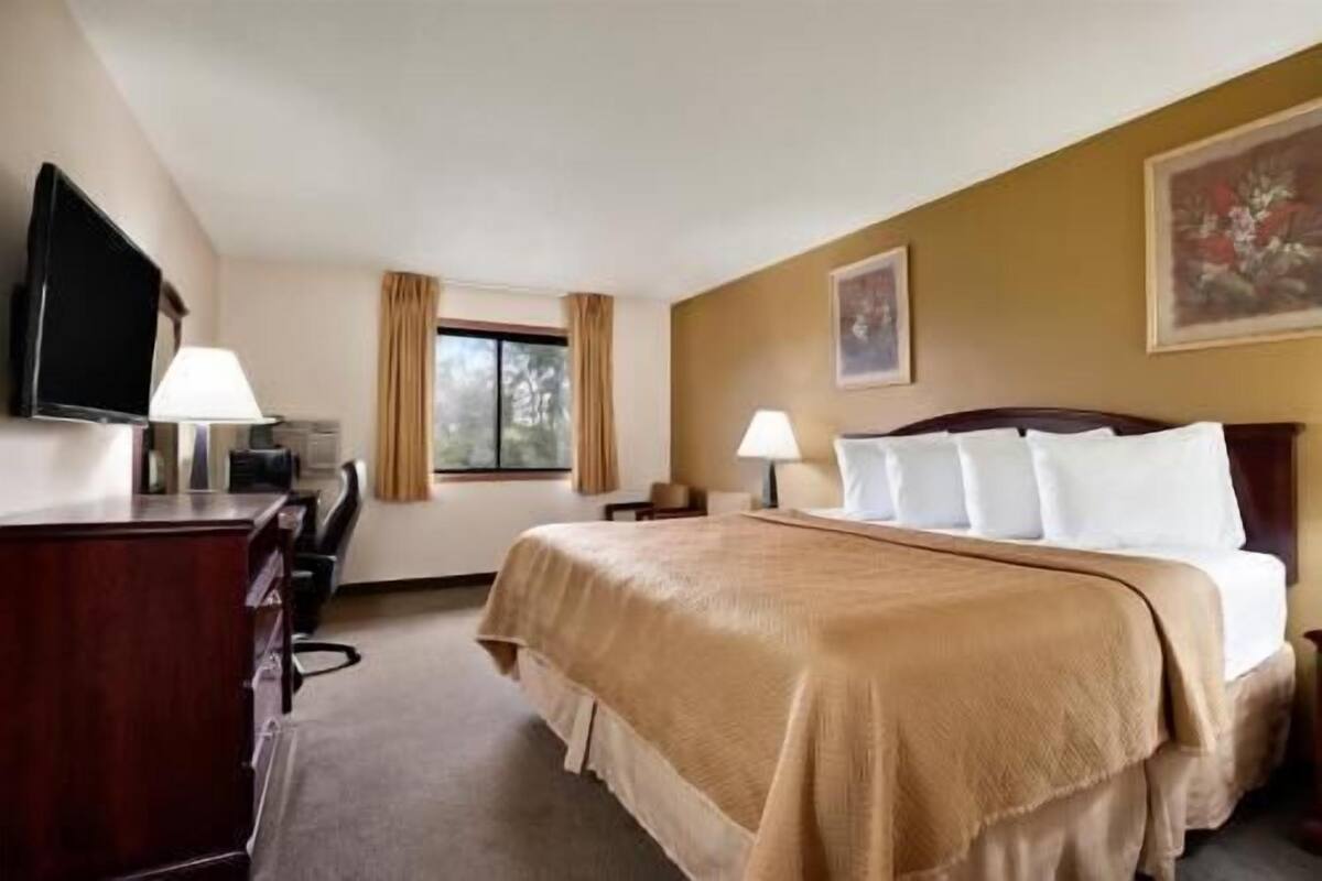 Une chambre d’hôtel avec un lit, un bureau, une chaise, une télévision et une fenêtre avec des rideaux.