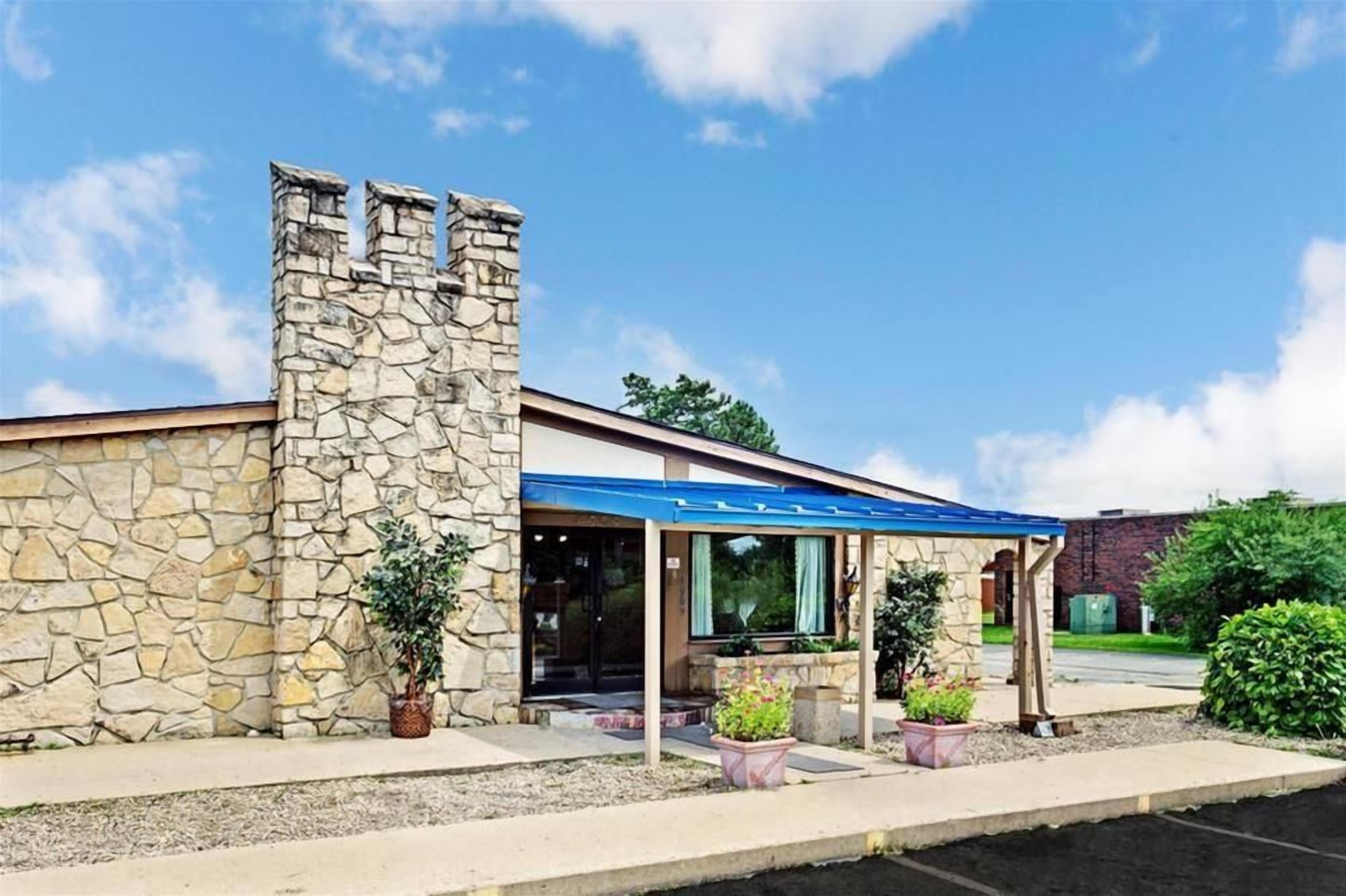Un edificio de piedra con un toldo azul, un acceso cubierto y plantas en macetas.
