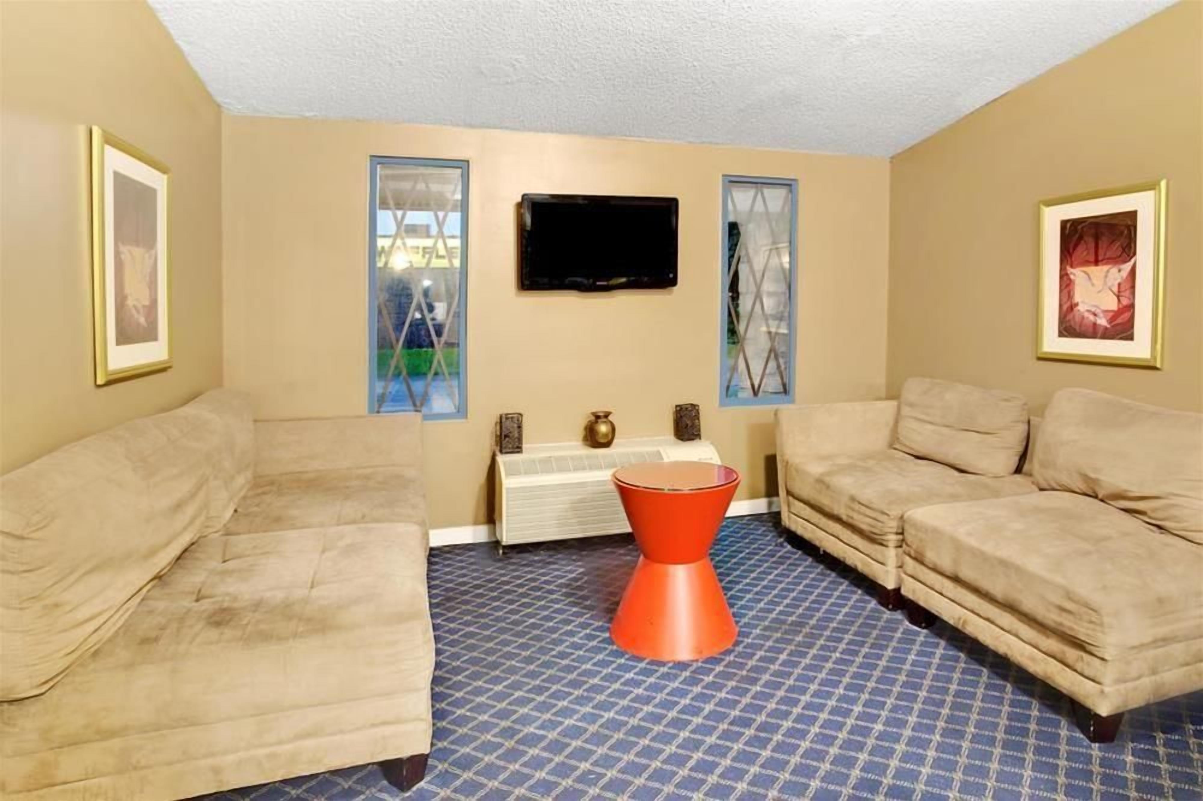A room with two beige sofas, a red stool, a flat-screen TV, and a radiator.