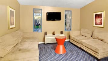 A room with two beige sofas, a red stool, a flat-screen TV, and a radiator.