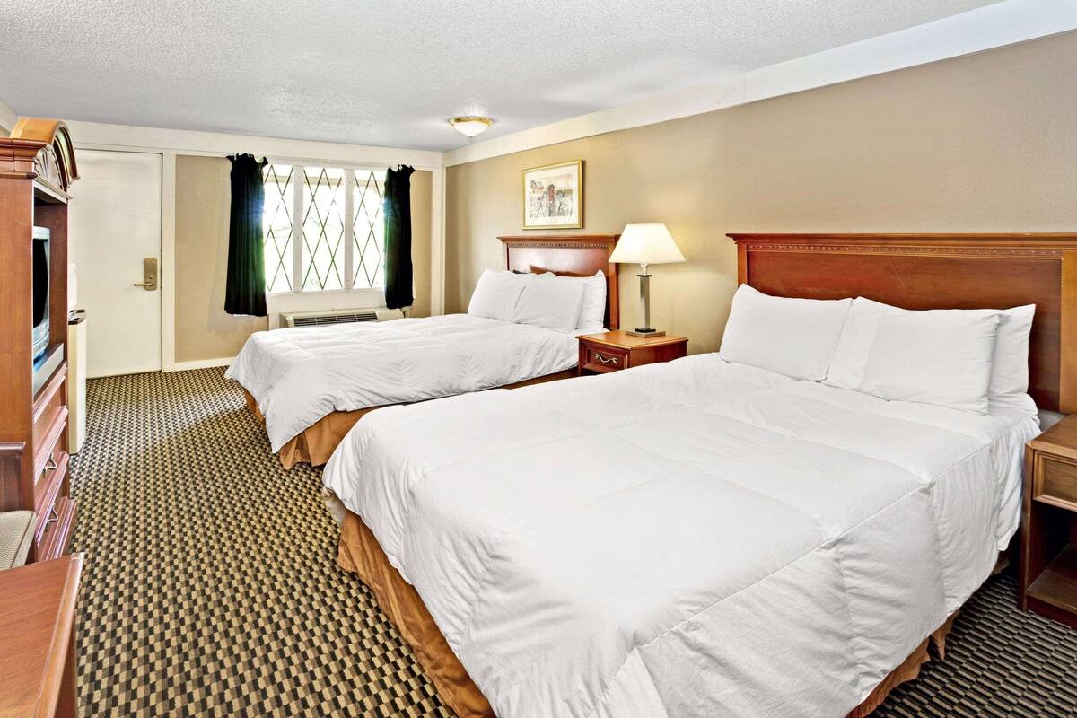 A hotel room with two beds, a desk, a lamp, and a window with curtains.