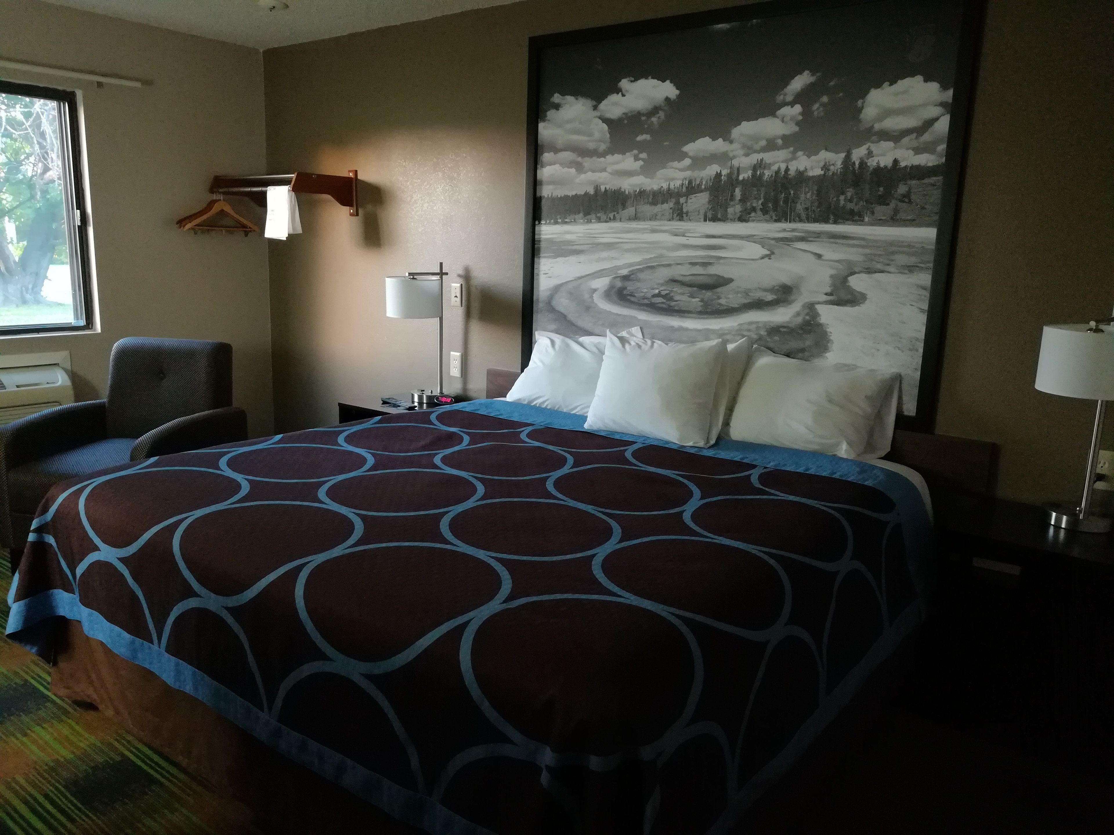 A hotel room with a large bed, a chair, a desk, a lamp, and a painting of a snowy landscape.