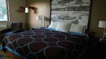 A hotel room with a large bed, a chair, a desk, a lamp, and a painting of a snowy landscape.