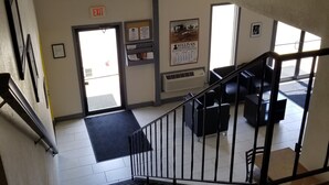 A staircase leading to a room with a black leather sofa, a framed picture on the wall, and a poster advertising an auction. - Super 8 by Wyndham Keokuk (Keokuk)