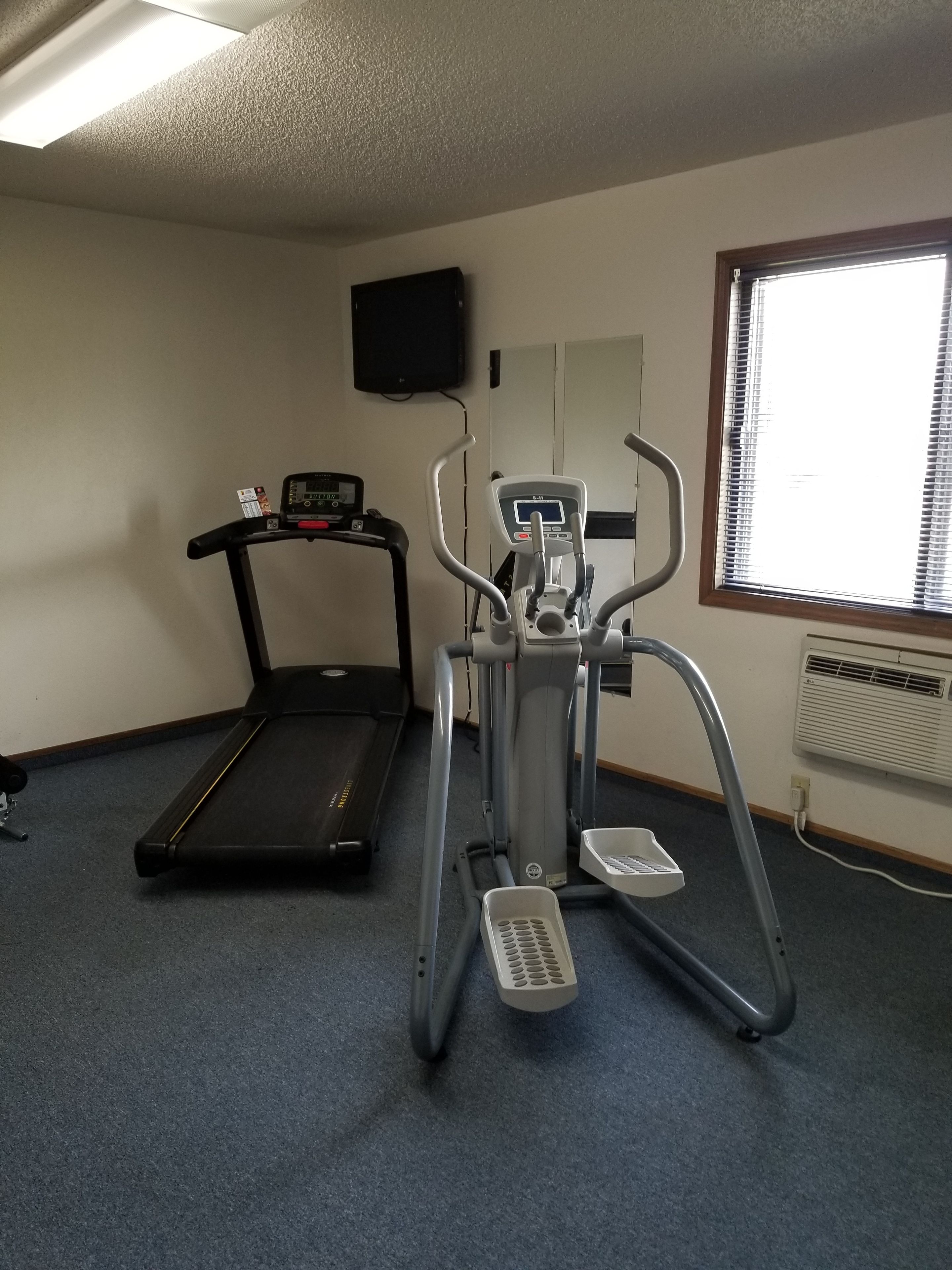 A fitness room with a treadmill and an elliptical machine.