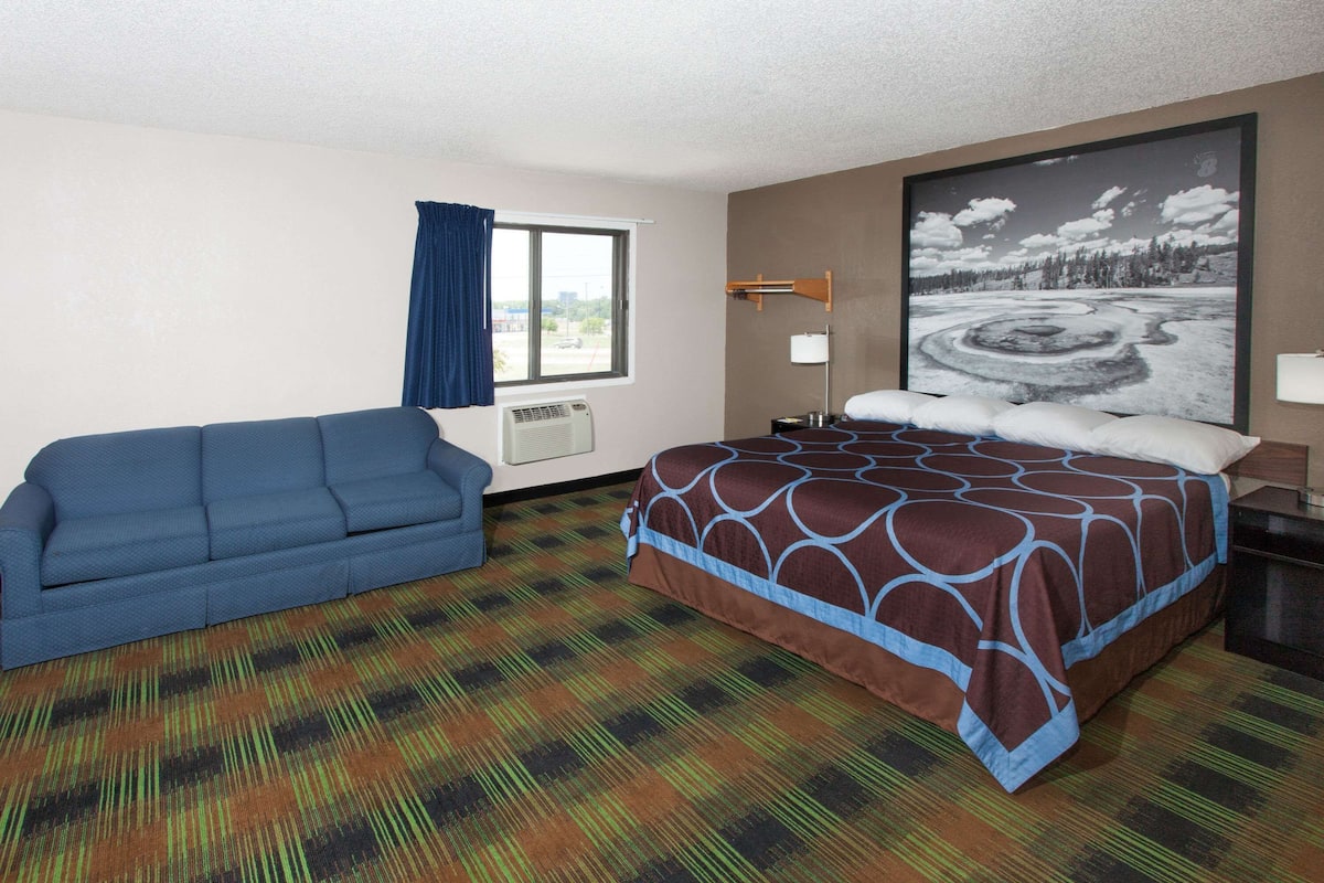 A hotel room with a bed, a blue sofa, a large window with a view, and a carpeted floor.