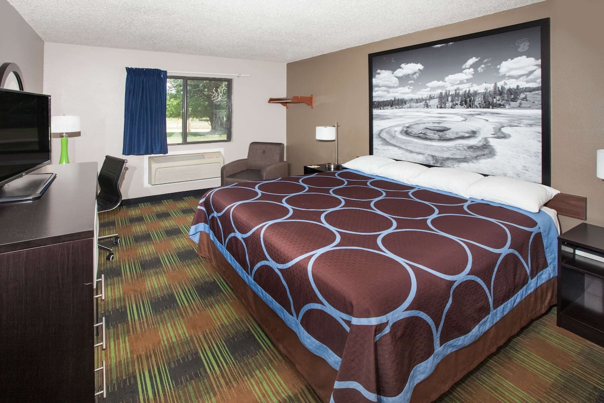 A hotel room with a large bed, a desk with a computer, a TV, and a window with curtains.
