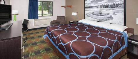 Habitación de hotel con una cama grande, un escritorio con computadora, televisor y ventana con cortinas.